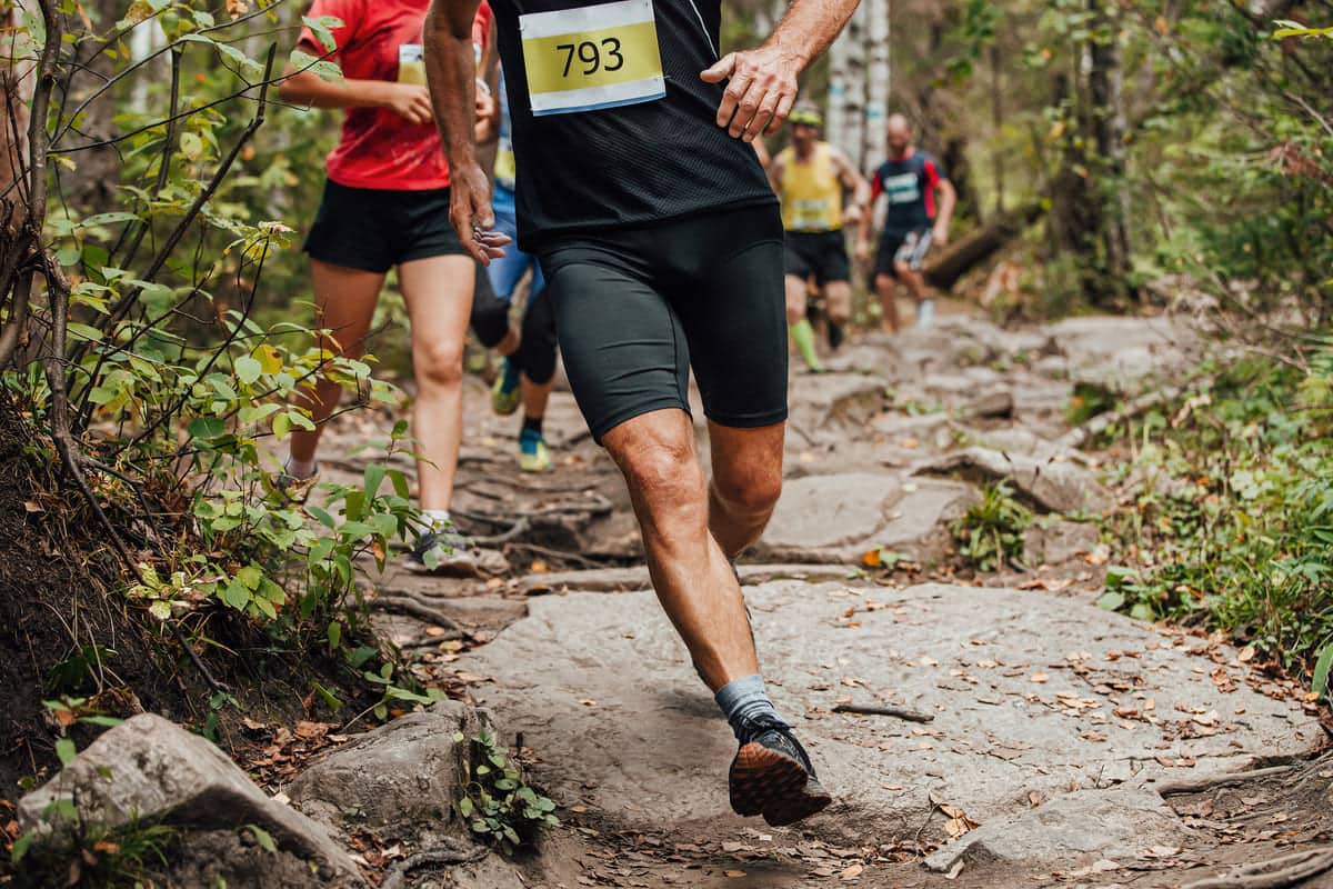 Coureurs dossard au trail sur un sentier rocheux en forêt